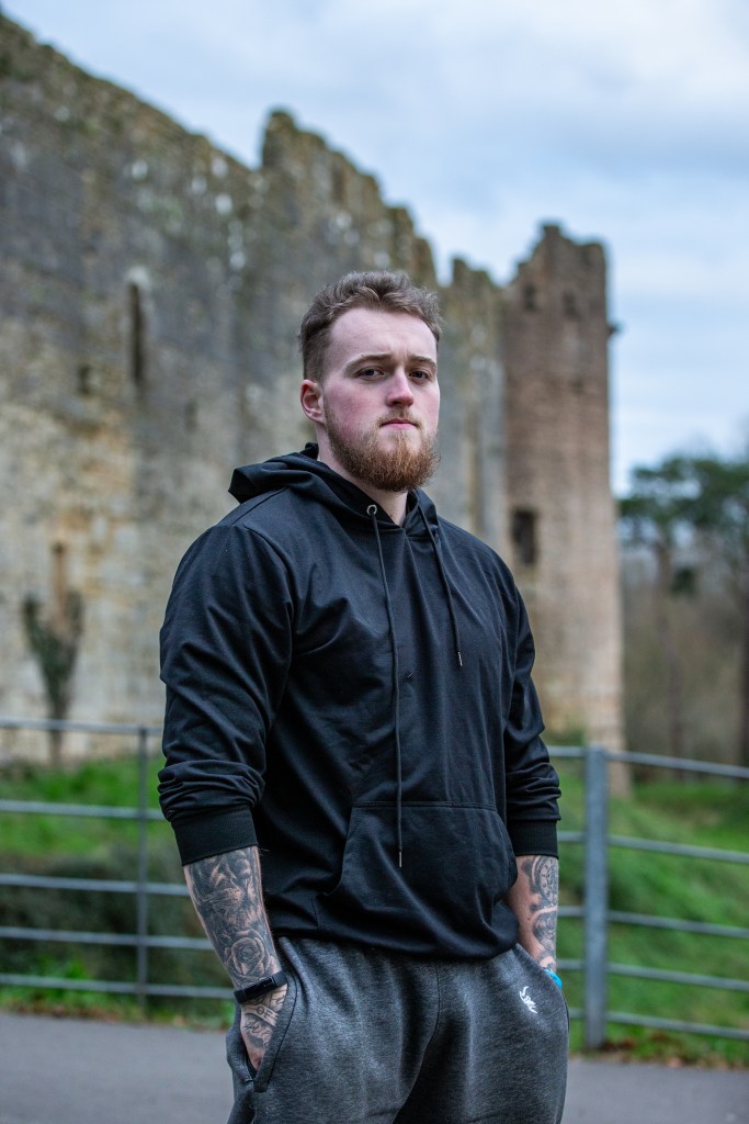 A man with a beard wearing a black hoodie standing in front of Caldicot Castle with his hands in his pockets